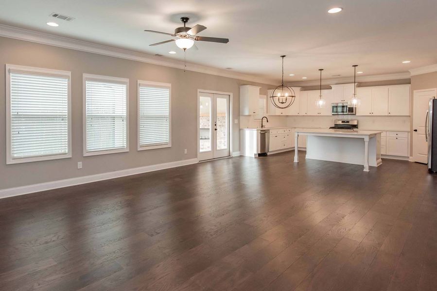 Spacious, open-concept living area with dark wood floors, white kitchen, and large windows.