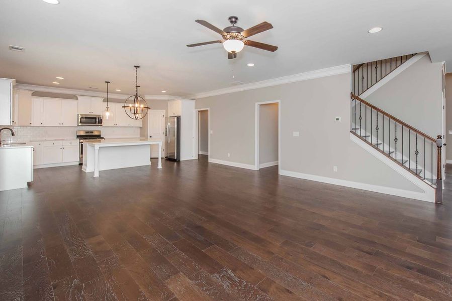 Open-concept living space with hardwood floors, white kitchen, staircase, and neutral walls.