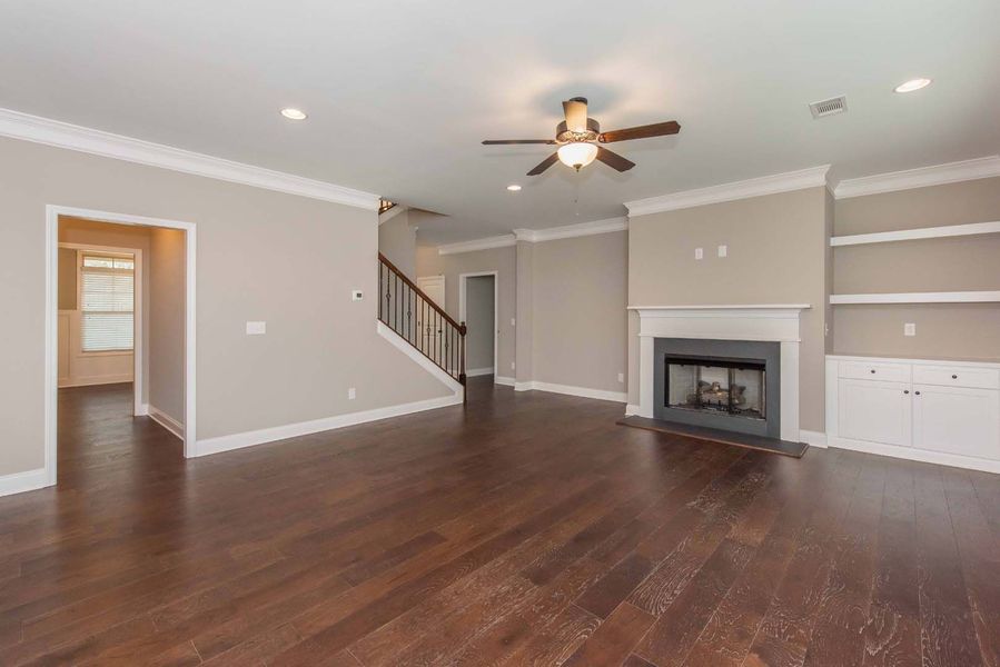 Spacious living room with dark wood floors, fireplace, built-in shelves, and a staircase.