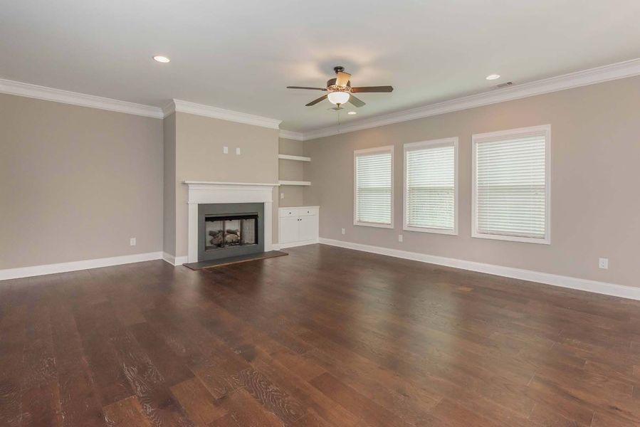 Empty living room with fireplace, dark wood floor, and tan walls.