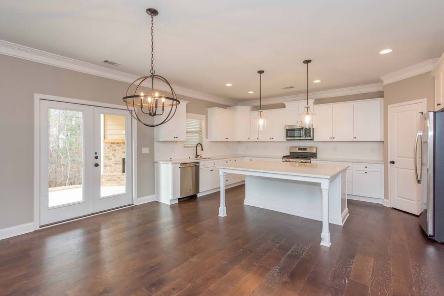 Spacious kitchen with white cabinets, island, and appliances; dark wood floors and French doors.