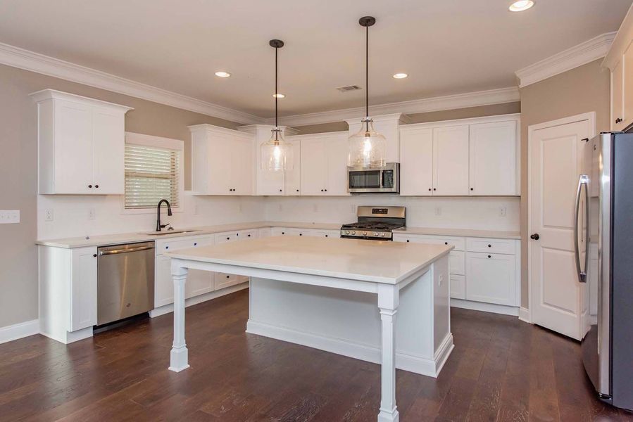 White kitchen with island, white cabinets, dark floors, stainless steel appliances.