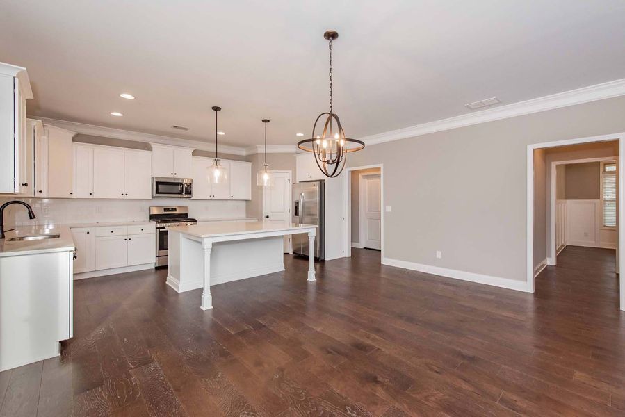 Kitchen with white cabinets, island, dark wood floor, and neutral walls; an open doorway leads to hallway.