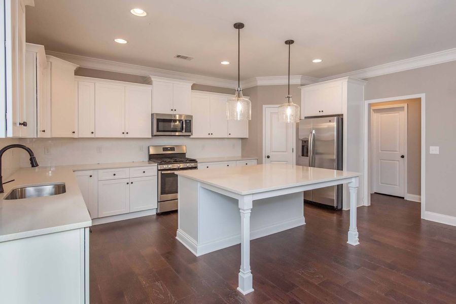 White kitchen with stainless steel appliances and a large island, dark wood floors.