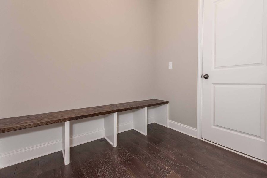 A wooden bench with white supports against a beige wall in a room with a door and wood flooring.