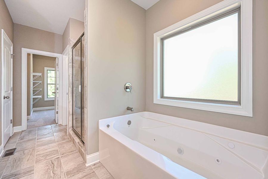 Bathroom with a white jacuzzi tub, large window, and beige walls. Doorways lead to other rooms.
