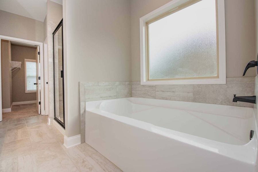 Modern bathroom with a white bathtub, shower, and frosted window.