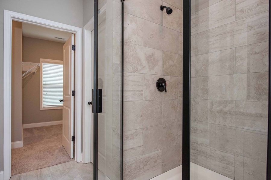 Bathroom with gray tiled shower, black fixtures, and a door leading to a closet.
