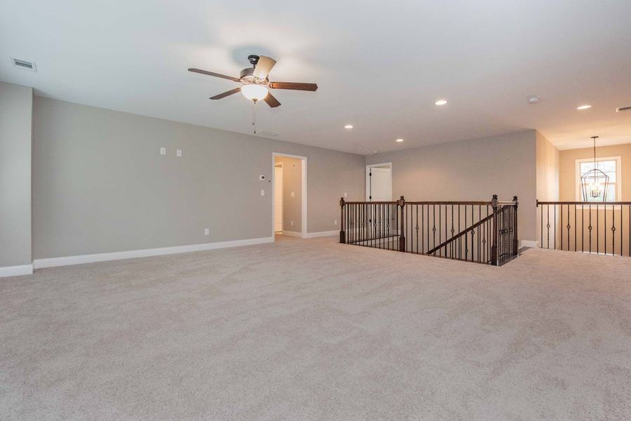 Spacious, neutral-toned loft area with carpet flooring, a staircase, and a ceiling fan.