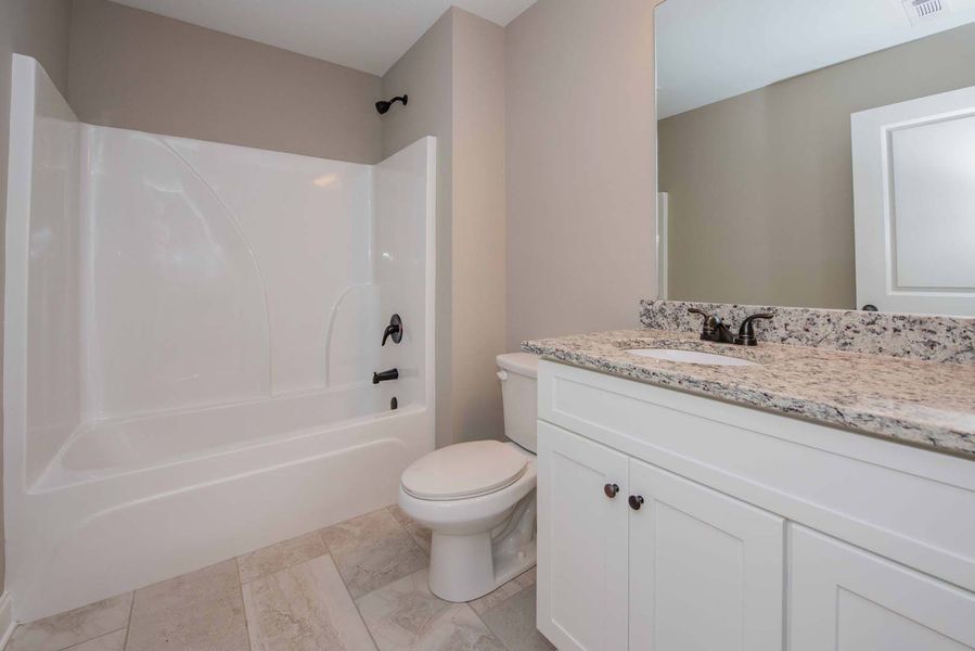 White bathroom with a tub, toilet, vanity with granite countertop, and light gray walls.