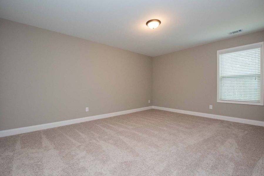 Empty bedroom with beige carpet, walls, and a window with blinds.