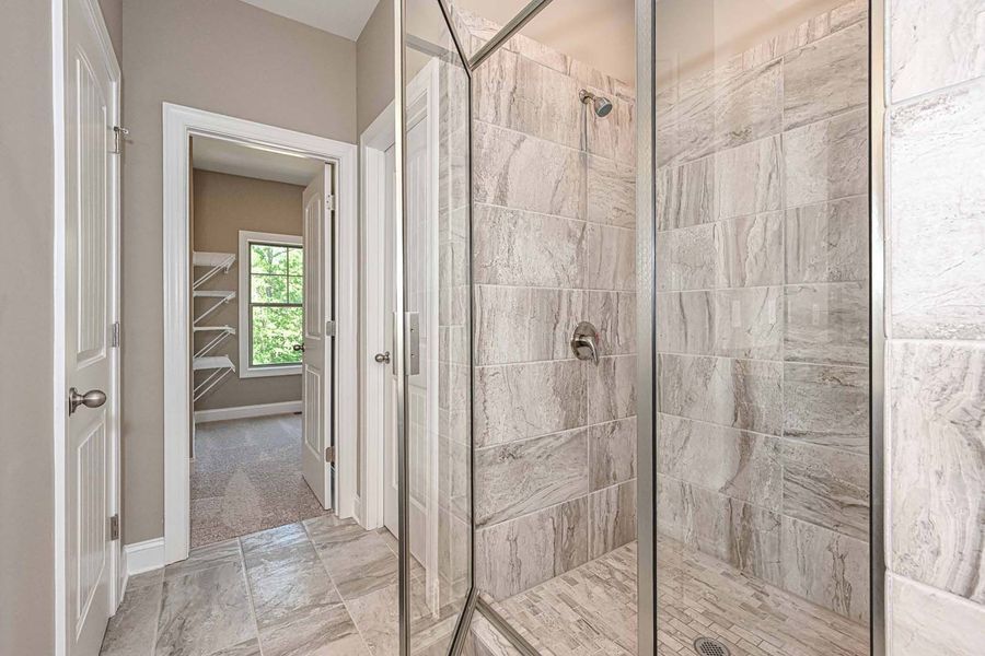Bathroom interior with a glass shower, tile walls, and a doorway to a bedroom.