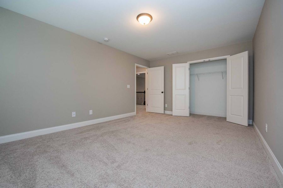 Empty bedroom with gray walls, beige carpet, and white closet doors.