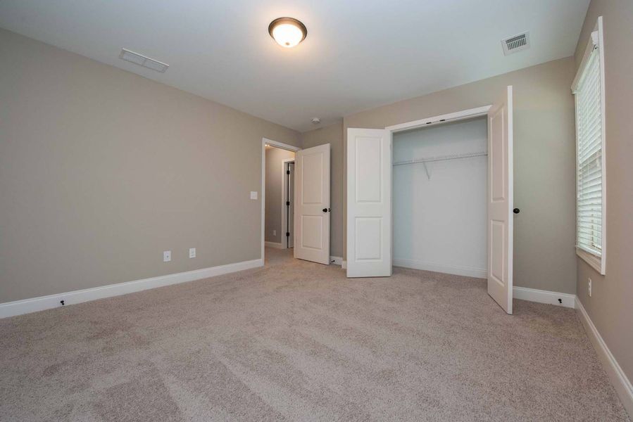 Empty bedroom with beige walls, carpet, closet, and open doors.