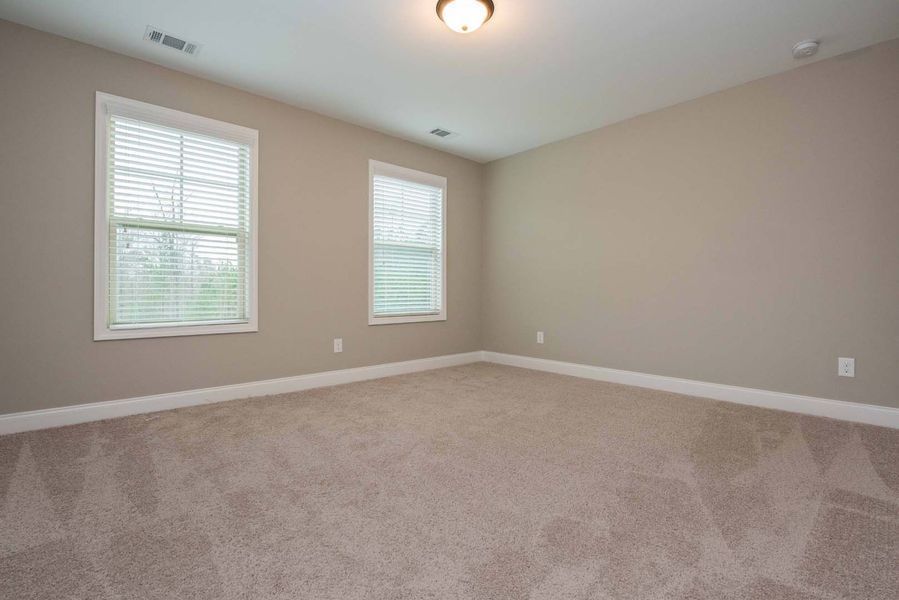 Empty bedroom with beige walls, carpet, two windows, and ceiling light.