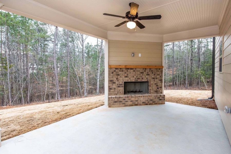 Covered patio with a brick fireplace, ceiling fan, and forest view.