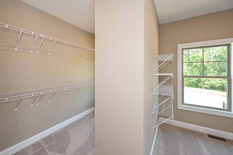 Walk-in closet with wire shelving on beige walls, window to the right, carpeted floor.
