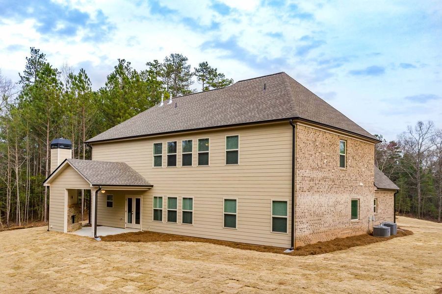 Two-story beige and brick house with a covered patio in a wooded setting.