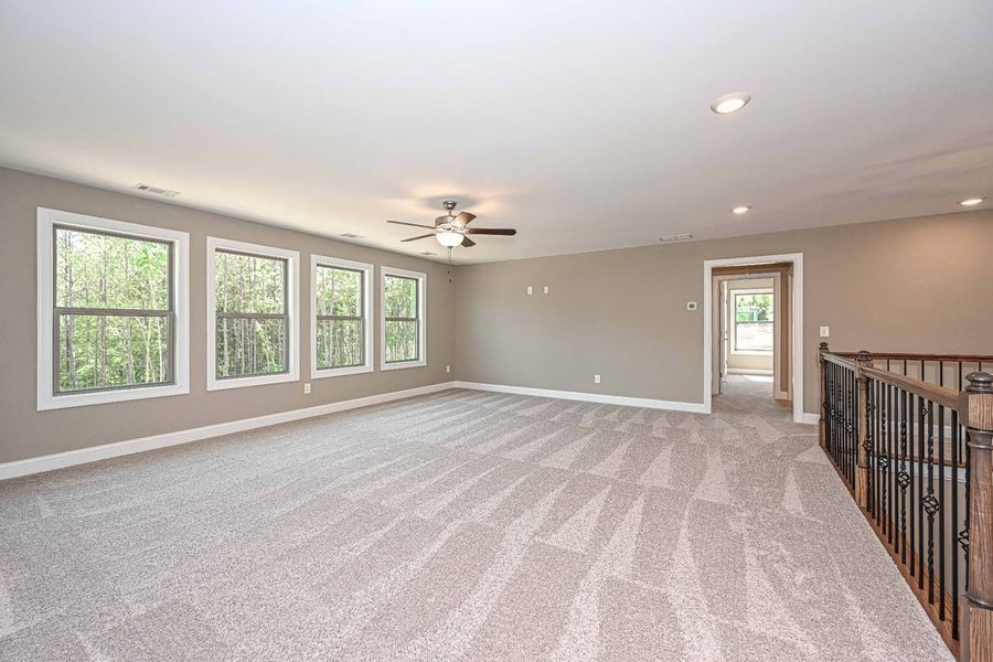 Spacious room with gray carpet, windows, and neutral walls. A doorway leads to another room, with a staircase railing.