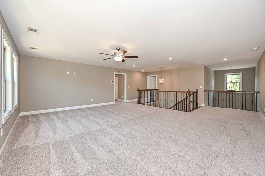 Spacious, carpeted bonus room with neutral walls and ceiling, open to a second-floor railing.