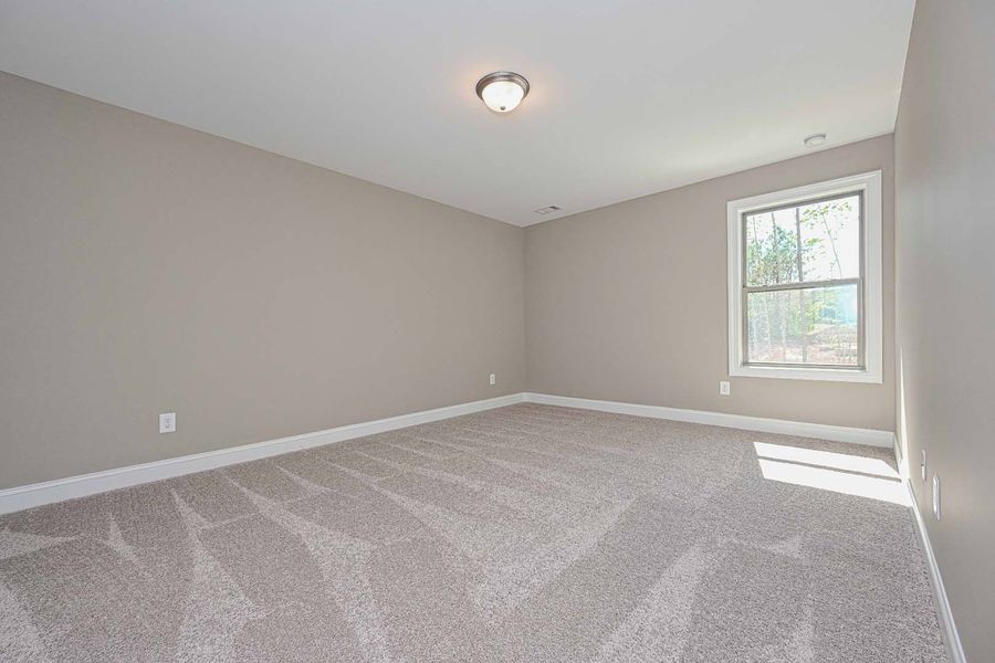 Empty bedroom with beige walls, patterned carpet, and a window.