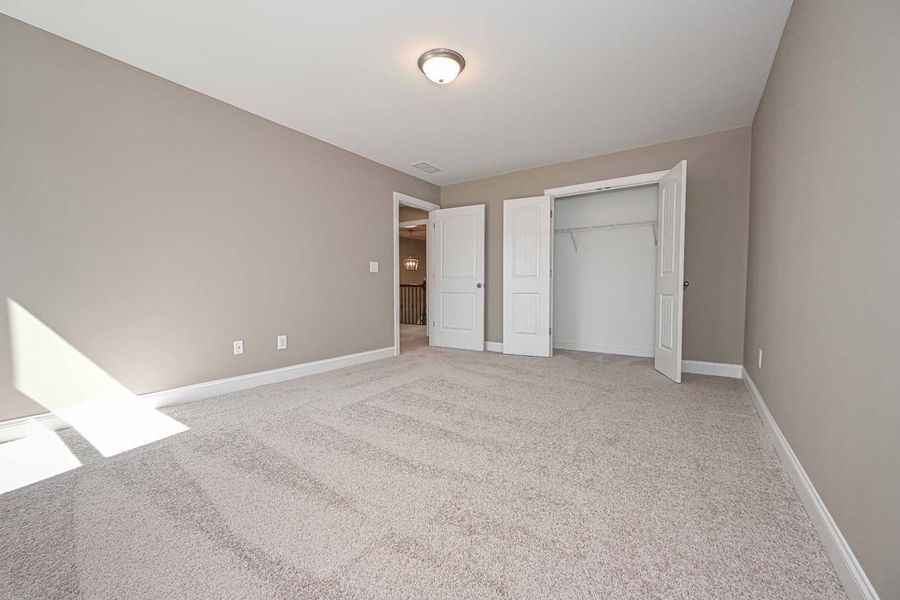 Empty bedroom with beige walls, carpet, closet, and a door to a bathroom.