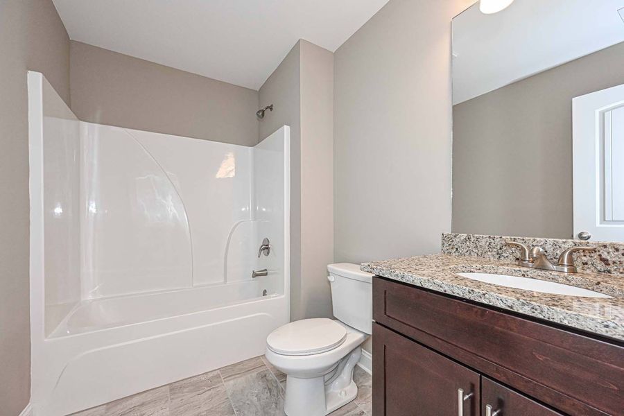 Bathroom with a white tub, toilet, brown vanity, and gray walls.