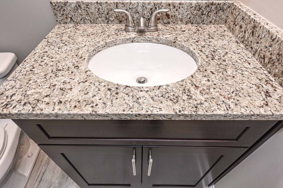 Bathroom vanity with oval sink, granite countertop, dark brown cabinet, and chrome fixtures.