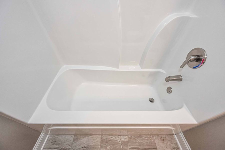 White bathtub and shower walls. Silver faucet. Gray floor.