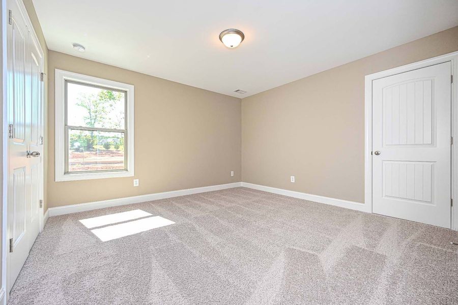 Empty bedroom with beige walls, white trim, and light gray patterned carpet.