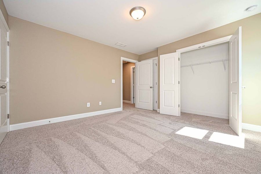 Empty bedroom with tan walls, white trim, carpet, and a closet.