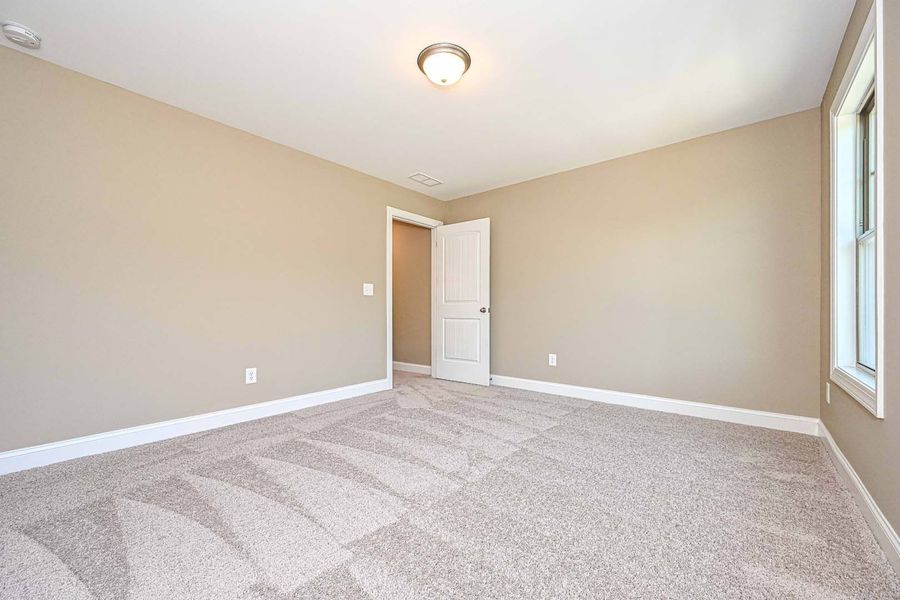 Empty beige bedroom with carpet, door, and a window.