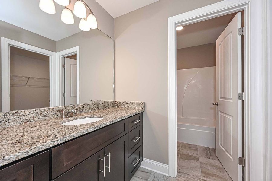 Bathroom with dark wood vanity, granite countertop, and a door to a tub/shower.