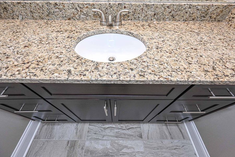 Bathroom vanity with granite countertop, oval sink, gray cabinets, and silver hardware.