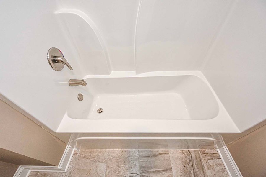 White bathtub in a white-walled bathroom with a silver faucet and neutral-colored floor tiles.