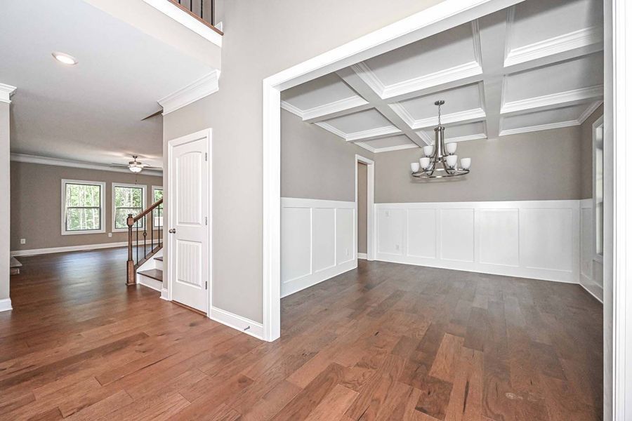 Entryway with hardwood floors, leading to a dining room with a white paneled wall and a chandelier.