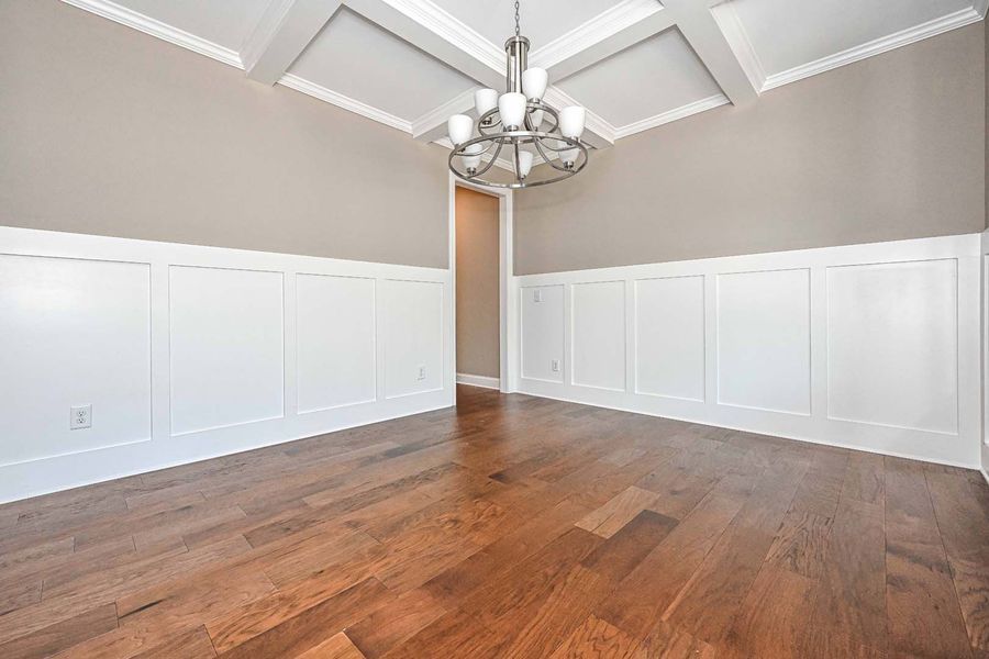 Empty room with wood floors, white paneling, and a chandelier.