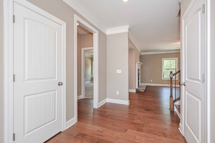 Hallway with hardwood floors, white doors, and neutral-colored walls.