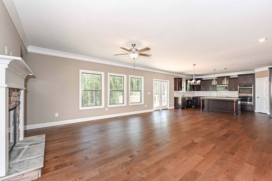 Open-concept living space with fireplace, windows, and kitchen; hardwood floors and neutral walls.