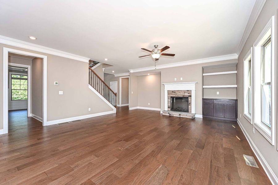 Spacious living room with hardwood floors, fireplace, built-in shelves, and staircase. Neutral tones and natural light.