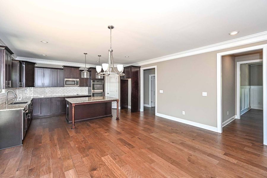 Open-concept kitchen with dark brown cabinets, island, and hardwood floors. A doorway leads to a hallway.