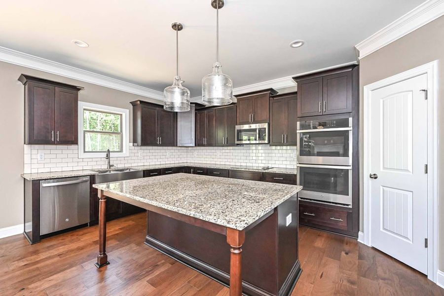 Dark wood kitchen with granite island, stainless steel appliances, and white tile backsplash.