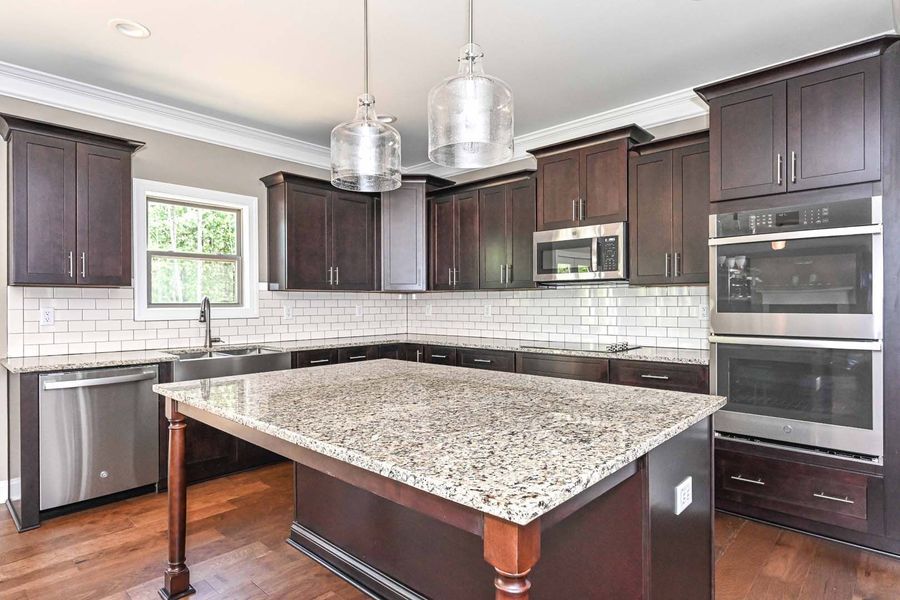 Modern kitchen with dark cabinets, granite island, stainless steel appliances, and hardwood floor.