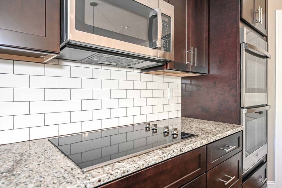 Kitchen with dark wood cabinets, white tile backsplash, granite countertop, and stainless steel appliances.