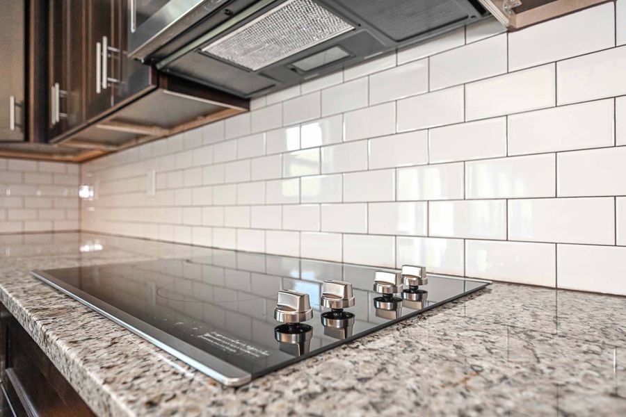 Modern kitchen with granite countertop, white subway tile backsplash, and glass cooktop.