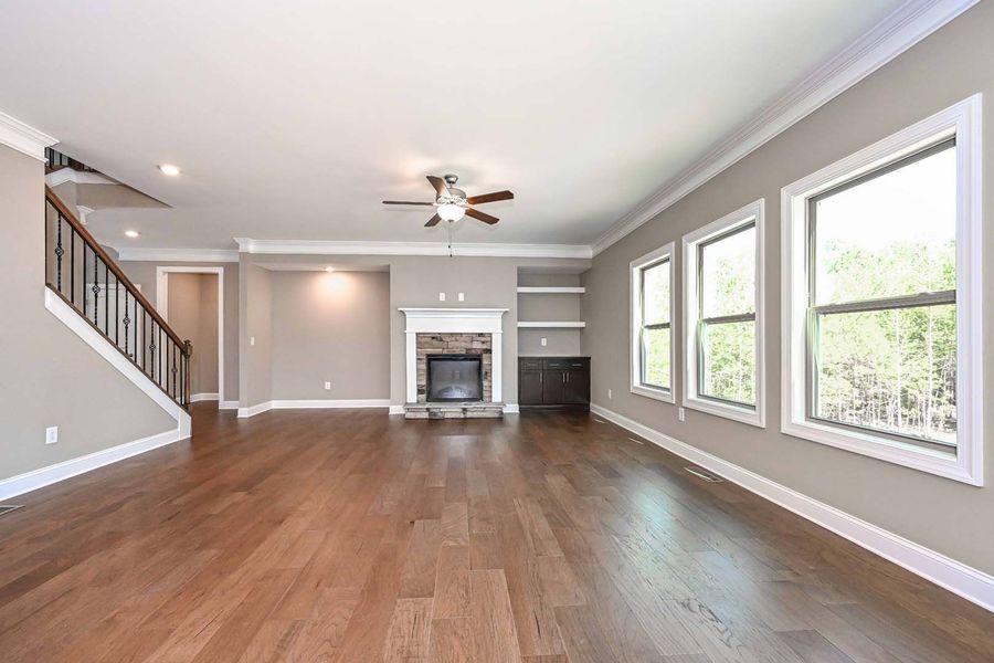 Spacious living room with hardwood floors, fireplace, windows, and staircase.