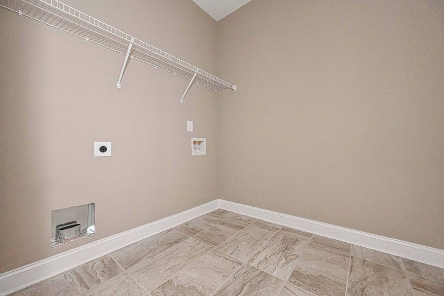 Empty laundry room with tan walls, tile floor, wire shelf, and utility hookups.