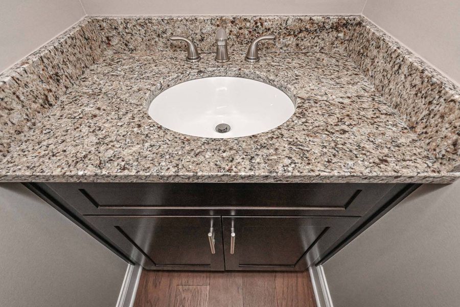 Granite countertop with oval sink, dark wood vanity with silver hardware.