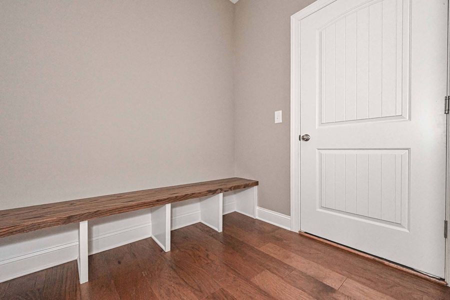 Wooden bench with storage below, next to a white door in a room with wood floors and neutral walls.