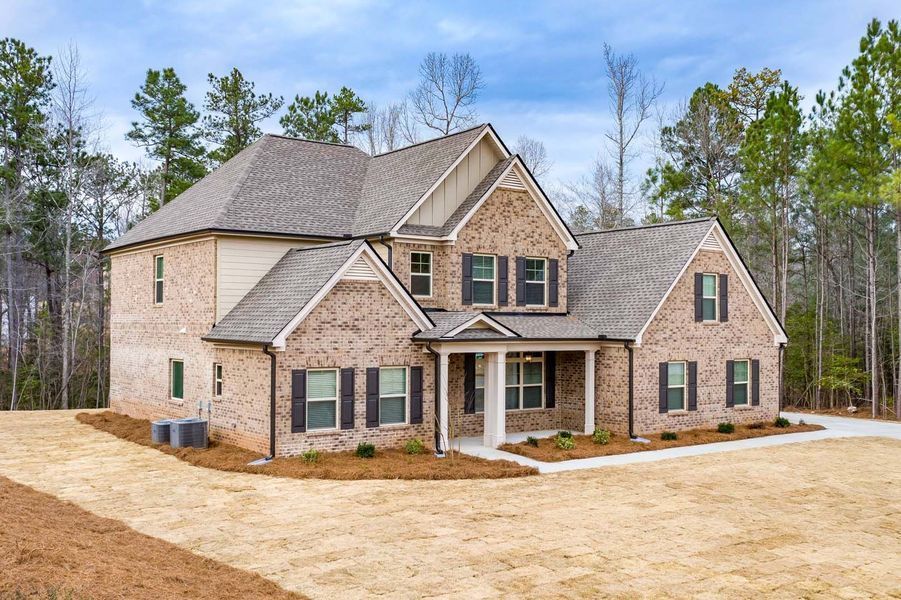 Two-story brick house with a brown roof and green shutters in a wooded area.